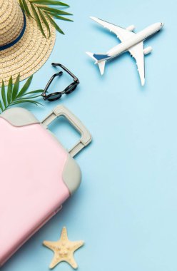 Seyahat aksesuarları konsepti pembe bavul, uçak modeli, güneş gözlüğü ve mavi arka planda fotokopi alanı olan hasır şapka