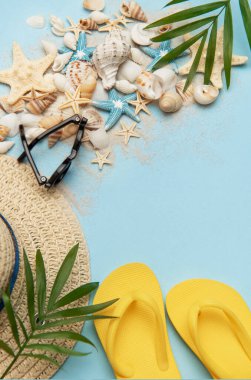 Deniz kabukları, güneş gözlükleri, parmak arası terlikler ve mavi arka planda hasır şapka olan yaz tatili plajı.