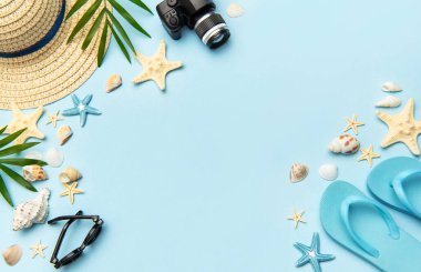 Terlik, güneş gözlüğü, kamera, deniz kabuğu, denizyıldızı ve hasır şapka gibi plaj aksesuarları açık mavi arka planda fotokopi alanı olan bir çerçeve oluşturuyorlar.
