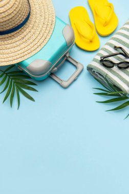 Bavullu yaz tatili konsepti, plaj havlusu, parmak arası terlik, güneş gözlüğü ve mavi arka planda fotokopi alanı olan hasır şapka.
