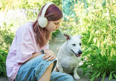 Kulaklıklı bir kız bahçede köpeğiyle etkileşime giriyor. Huzurlu bir bağ anının tadını çıkarıyor.