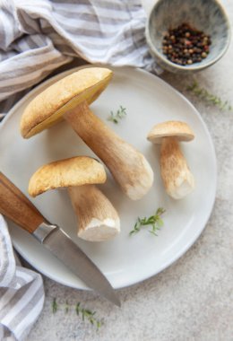 Taze toplanmış çörek mantarları beyaz bir tabakta, pişirilmeye hazır ve baharatlı otlar ve biberlerle