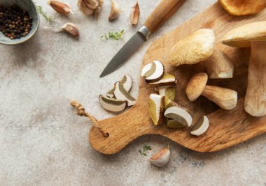 Taze biçilmiş mantarlar ahşap bir kesim tahtasının üzerinde dilimleniyor. Yanında sarımsak, biber ve kekik var. Lezzetli bir mutfak yaratımı için hazır.