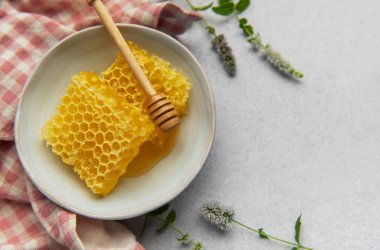 Taze bal peteği ve bal kabının içinde açık gri arka planda taze nane filizi.