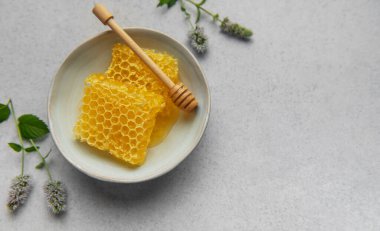 Altın bal peteği ve bal kovanı seramik bir kasede, taze nane filizi eşliğinde, doğal ve davetkar bir sahne yaratıyor.