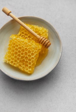 Altın bal peteği ve ahşap bal kovanı seramik bir kasede oturur, tatlı bir ikram için hazır.