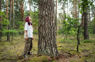 Gençler doğanın tadını çıkarıyor, yeşil bir ormanda büyük bir ağacın yanında duruyor, derin bir nefes alıyor.