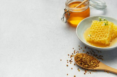 Altın bal, bal peteği ve arı poleni hafif bir arkaplanda lezzetli ve sağlıklı bir kompozisyon oluşturuyor.