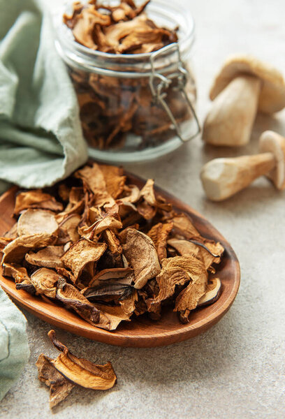 Dried porcini mushrooms spilling from a wooden plate, with fresh porcini and a jar of dried mushrooms in the background