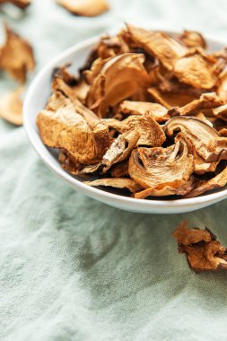 Yeşil bir kumaş üzerinde bir kase kurutulmuş mantarın yukarıdan görünüşü korunmuş mantarların dokusunu ve toprak tonlarını sergiliyor.