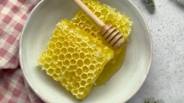 Balpeteği ve ahşap bal kovası bir kasede dinleniyor, yanında pembe gingham peçetesi ve taze nane filizi var.