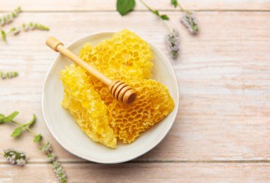 Ballı kase içinde taze bal peteği ve ahşap masada nane, doğal tatlandırıcı ve sağlıklı yiyeceği temsil ediyor.