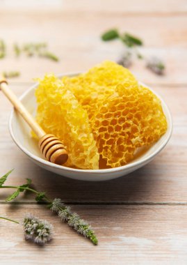 Ballı kase içinde taze bal peteği ve ahşap masada nane, doğal tatlandırıcı ve sağlıklı yiyeceği temsil ediyor.