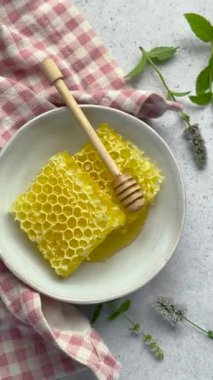 Balpeteği ve ahşap bal kovası bir kasede dinleniyor, yanında pembe gingham peçetesi ve taze nane filizi var.