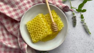 Balpeteği ve ahşap bal kovası bir kasede dinleniyor, yanında pembe gingham peçetesi ve taze nane filizi var.