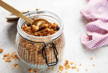 Yulaflı granola ve cam kavanozda kurutulmuş meyve, bir porsiyon altın kaşık.