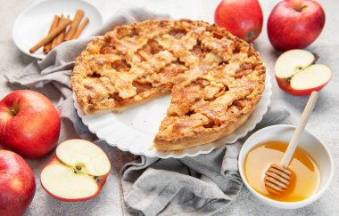 Taze elmalar, tarçın çubukları ve balla çevrili bir dilim eksik elmalı turta.