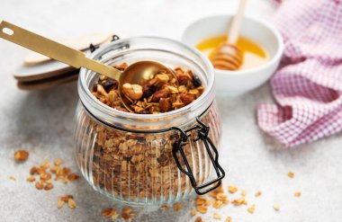 Yulaflı granola ve cam kavanozda kurutulmuş meyve, bir porsiyon altın kaşık.