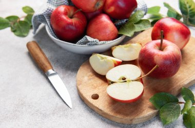 Fresh red apples, some sliced on a wooden cutting board, with a knife and a bowl of fruit