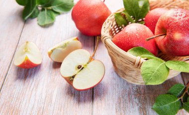 Su damlalı kırmızı elmalar ve tahtadan bir sepetin içinde yapraklar.