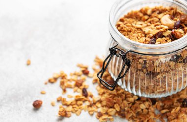 Hafif arka planda cam bir kavanozda yulaf ve fındıklı ev yapımı granola.