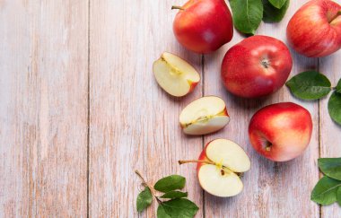 Taze kırmızı elmalar ve yeşil yapraklı kesikler kırsal bir ahşap yüzeyde yatıyor.