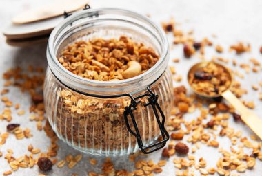 Cam bir kavanozu ölçü kaşığı ve dağınık malzemelerle dolduran ev yapımı granola.
