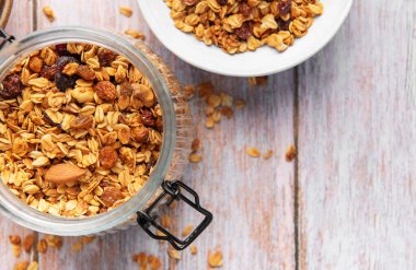 Cam kavanozda yulaf ve fındıklı tahıl gevreği ve tahta arka planda bir kase.