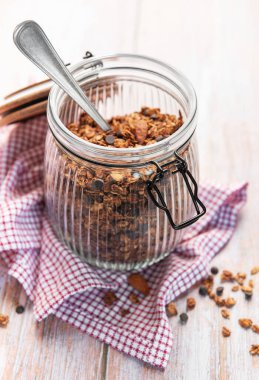 Fındıklı granola, çikolata parçacıkları ve tahta bir masada cam bir kavanozda kaşık.