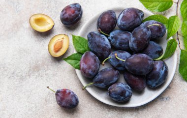 Taze toplanmış yeşil yapraklı erikler taştan arka planda sağlıklı organik meyveler sergiliyor.