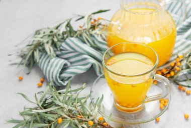 Deniz dikenli üzümler ve dallar bir fincanın etrafına dizilmiş ve çaydanlık ile sağlıklı böğürtlen çayı