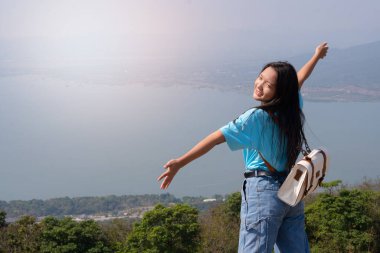 Sırt çantalı, şapkalı ve dağlara bakan genç bir kız ve dağda rüzgar türbini, yazı için yer, Khao Yai Thieng Tayland.