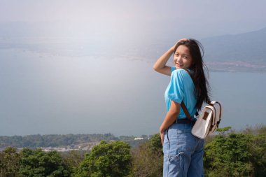 Sırt çantalı, şapkalı ve dağlara bakan genç bir kız ve dağda rüzgar türbini, yazı için yer, Khao Yai Thieng Tayland.