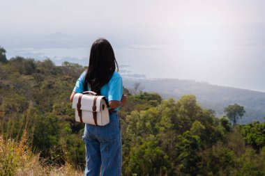 Sırt çantalı, şapkalı ve dağlara bakan genç bir kız ve dağda rüzgar türbini, yazı için yer, Khao Yai Thieng Tayland.