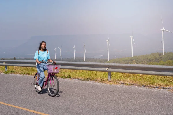 若い女の子は 風力タービン テン電気風力タービンタイで山の道に自転車に乗る — ストック写真