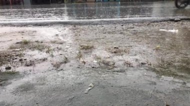 Su birikintisindeki yağmur damlaları. Şiddetli bir sağanak yolu ıslattı ve insanların araçları yoldan geçti. 4K video.