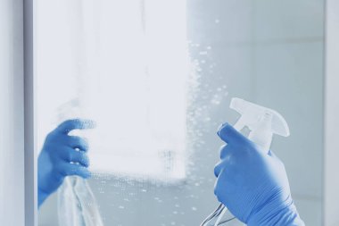 Kâhya kadının elinde lastik mavi eldivenlerle aynaya kimyasal temizleyici sıkarken evdeki banyoyu temizlediği görüntüler. Oda servisi ve temizlik servisi. Ev temiz, temizlik temiz.
