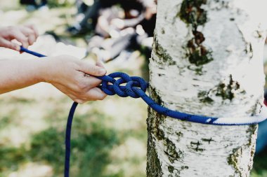 Kadın elleri bir huş ağacına bağlanmış güçlü mavi bir ipi çeker. Profesyonel teleferik hattı ya da teleferik kurulumu. Eğlence ve rahatlama zamanı. Hafta sonları aile aktiviteleri. Yüksek kalite fotoğraf