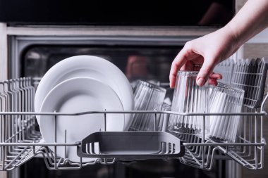 Kadın el doldurma, boşaltma ya da bulaşık makinesini çatal bıçak ile boşaltma. Mutfak aletleri, yaşam tarzı manzarası. Kadın bulaşık makinesine bir tabak koyar ya da ondan alır. Ev hanımı ev işlerini yapar. 