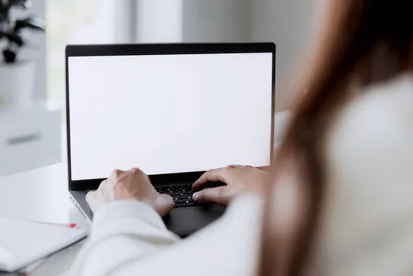 Kadın elleri boş beyaz ekran modeliyle dizüstü bilgisayarda yazıyor. Bilgisayar beyaz masanın üzerinde yatıyor. Arka plan bulanık. Ev konseptiyle çalışan biri. Metin için alanı kopyala