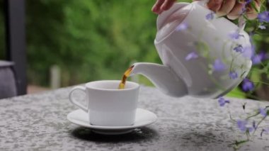 Elinizi kapayın ve seramik çaydanlıktan bir bardağa kadar siyah çay veya kahve doldurun. Yazın açık hava. Cafe veya restoran terasında garsonluk yapan bir müşteri. Yüksek kaliteli FullHD görüntüler