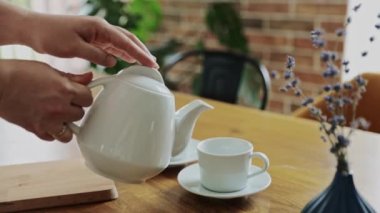 Hand is pouring hot drink from teapot into two tea cups, mugs indoors. Relaxing time at home or in cafe or restaurant. Waiter serving customers. Business with good service. High quality FullHD footage