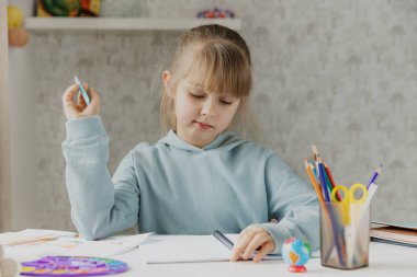 Okullu şirin küçük kız, elinde kalemle yatak odasında oturuyor, ödev yapıyor, evde ders çalışıyor, sınavlardan önce hazırlanıyor, notlar yazıyor. Evde eğitim, evde eğitim.