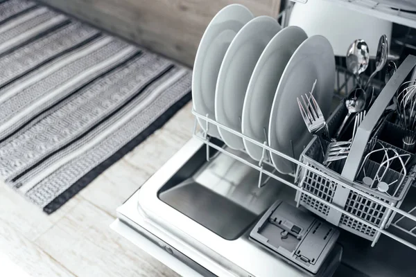 Modern ev mutfağının içinde temiz aletlerle otomatik paslanmaz bulaşık makinesinin kapanışı. Beyaz tabaklar, tabaklar, metal çatallar ve bıçaklar. Ev işleri, ev işleri, ev işleri.