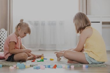 Çocuklar renkli plastik yapı taşlarıyla oynarlar. Çocuklar evde, yatak odasında, anaokulunda, çocuk odasında yerde oturuyor. Eğitici çevre dostu çocuk oyunu. Sevimli küçük kız kardeşler birlikte eğleniyorlar.