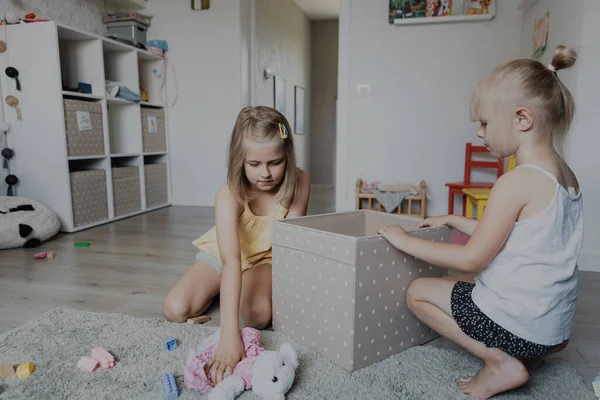子供たちは遊んだ後 床からおもちゃを掃除し それらを繊維箱に集めます 白い家の寝室 幼稚園の遊び場または遊び場の中心でカーペットの上に座っている子供 教育環境に優しいゲーム — ストック写真