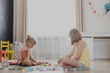 Çocuklar renkli plastik yapı taşlarıyla oynarlar. Çocuklar evde, yatak odasında, anaokulunda, çocuk odasında yerde oturuyor. Eğitici çevre dostu çocuk oyunu. Sevimli küçük kız kardeşler birlikte eğleniyorlar.