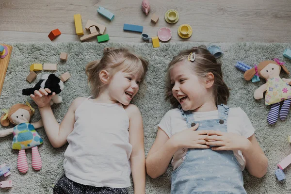 上からのトップビューは カラフルなおもちゃで遊んでいる子供たち 自宅の寝室や幼稚園でカーペットの上に横たわっている子供たちの肖像画 2人の笑顔の姉妹 教育環境に優しいゲーム — ストック写真