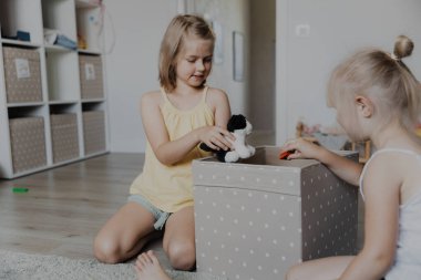 Çocuklar oyun oynadıktan sonra yerden oyuncakları temizler, onları tekstil kutusuna toplarlar. Beyaz ev yatak odasında, anaokulunda ya da çocuk parkında halı üzerinde oturan çocuklar. Eğitici çevre dostu oyunlar