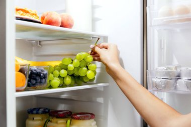 Kadın el ele tutuşuyor, açık buzdolabından üzüm topluyor ya da içi meyve, yabanmersini ve yoğurt dolu buzdolabı çekmecesinden üzüm topluyor. Sağlıklı beslenme, yaşam tarzı konsepti